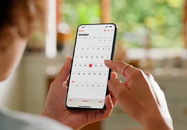 Close-up of a hand holding a smartphone displaying a calendar app, with another hand tapping a date in October to schedule or manage an appointment.